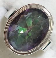 Close-up shots of the ring showing the oval mystic topaz stone with visible facets and the sterling silver bezel setting and band.