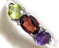 Close-up angled view of the ring showing the green peridot, central red garnet, and purple amethyst stones in the sterling silver setting.