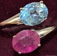 Close-up of the oval blue topaz and ruby gemstones set in sterling silver band, showing the faceting and color of the stones.