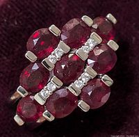 Close-up photo of sterling silver ring with oval-cut ruby gemstones and diamond accents on a dark background, showing stone arrangement and setting