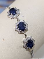 Close-up of three oval blue sapphires each surrounded by small clear stones in a starburst sterling silver setting