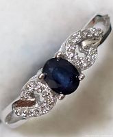 Close-up front view of sterling silver sapphire and cubic zirconia ring showing oval blue sapphire center and CZ set decorative sides.