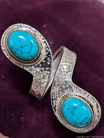 Close-up photo showing the hammered texture silver ring with two prominent oval turquoise stones, placed on a dark purple cloth.