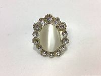 Close-up of the costume jewelry ring with visible oval white stone and surrounding clear rhinestones