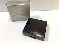 Closed compact with reflective dark surface, Laura Mercier logo on cover, and original silver packaging box.