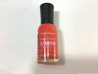 Single bottle of Sally Hansen Xtreme Wear Hard As Nails nail polish in coral/orange shade with black cap.