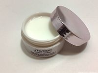 Open jar showing white cream inside with light pink metallic lid next to it.