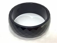 Black faceted cuff bracelet angled to show geometric diamond and triangle patterned facets and high polish finish.