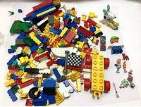 Photo showing a pile of assorted brightly colored Lego blocks and bricks along with several small toy figures including a white Snoopy figure and a Lego person.