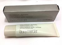 Photo showing Laura Mercier Illumination Tinted Moisturizer tube next to its silver box, front facing with branding and product name visible.