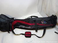 Side view of the black and red Ping golf shaft travel bag showing the zippered compartments and attached wheels.