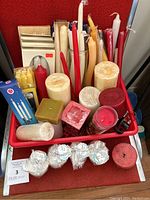 Overview of assorted candles in a red container showing various shapes, sizes, and colors.