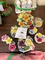 Overhead view of seven vintage porcelain floral figurines arranged on a wooden surface, showing various colorful flowers in small porcelain bases.