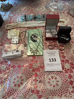 Photo of assorted necklaces, earrings, rings, and jewelry boxes on a lace cloth.