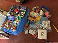 Overview of lot with toys, stuffed animals, bedding, and art supplies on and around blue storage bin