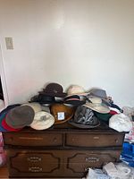 Photo of approximately 16 vintage ladies' winter hats arranged on a wooden dresser, showing a variety of colors, styles, and materials.