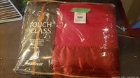 Photo of the acrylic blanket in original packaging showing branding and part of the red blanket material.