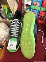 Pair of Nike Air Force 1 shoes laid out with tops and soles visible. Black and dark grey uppers with white swoosh and white laces. Neon green translucent soles showing circular tread pattern.