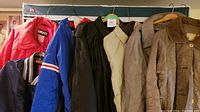 Front view of various outdoor jackets and coats hanging on a rack, showing color and style differences