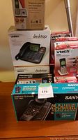 Photo showing multiple boxed telephones stacked together including Uniden desktop, Panasonic, VTech, and Sanyo models