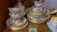 Photo showing stacked plates, cups, saucers, creamer and gravy boat with lavender rose floral pattern and gold trim.