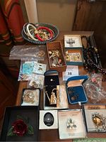 Overview of entire lot arranged on wooden surface showing bracelets in oval dish, boxes of brooches and earrings, necklaces, rings and loose pendants.