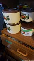 Four vintage Sterilite plastic canisters with brown lids and vegetable motif on the side, stacked on a wooden shelf.
