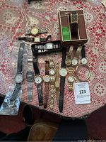 Top view of all 16 vintage ladies watches arranged on table showing different strap materials and dial shapes.