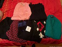 Photo showing six sweaters laid out on a red surface featuring pink, black, teal and patterned designs.