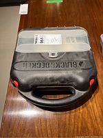 Closed black plastic Black & Decker carrying case with handle and logo on top.