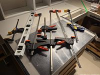 Photo shows 36 inch white metal spirit level with three bubble vials and six IRWIN Quick-Grip clamps arranged on table.