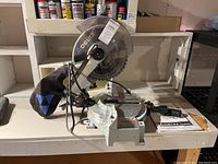 Full left-front view of miter saw on workbench with manual and clamp visible