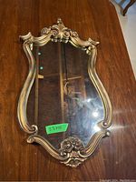 Front view of the gilded frame mirror showing ornate scrolling design and reflective glass surface with size label 23x13.