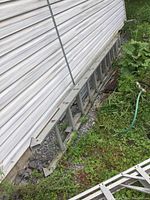 Full view of the aluminum 18 ft extension ladder lying on the ground near a building with visible weathering, dirt, and vegetation around it.