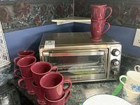 Hamilton Beach toaster oven with 10 red coffee mugs stacked around and on top on a kitchen counter.