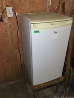 Front and side view of the white Danby Designer bar fridge placed on a small table, showing some dirt accumulation and measuring stickers.