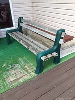 Photo showing full bench with green resin ends and weathered wooden slats on an outdoor deck area with green outdoor carpet and siding in background.
