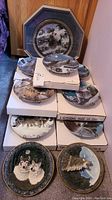 Full view of the collection showing several wolf plates stacked on original boxes and the framed larger plate behind.