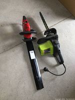 Full overview of both electric tools, Poulan electric chainsaw and red Toro electric hedge trimmer laid on the floor.