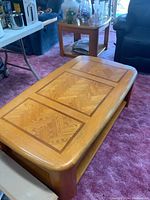 Coffee table in the foreground with inlaid wood panels on top and lower shelf, showing solid wood frame and some wear on front edge.