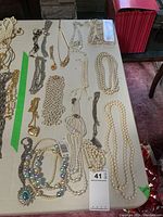 Photo of a variety of costume jewelry pieces including multiple faux pearl strands, metallic chains, and pendants laid on a table.