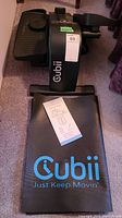 Cubii Jr seated elliptical black unit shown from the side with manufacturer's label and included manual on top, placed on carpet.