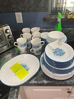 Eight mugs with blue rose pattern on white glass, stacked and grouped on countertop