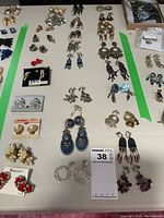 Full display of assorted clip-on costume earrings laid out on a table with green tape borders and a lot number card visible
