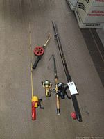 Four fishing poles laid out on floor: extendable with damaged reel, ice fishing pole with red circular reel, kids pole with yellow/red handle, and black spinning rod.