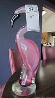 Front right angled view showing pink glass flamingo with clear round base and black beak with white accent, labeled with size tag.