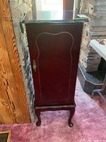 Side and front view of a wooden jewelry stand showing the door facing out, with a metal door handle and curved legs.