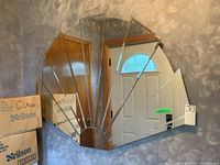 Sunburst mirror reflecting a door and boxes in the background. Shows the fan-shaped layout of the mirror segments and its bevel-edged finish.