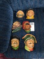 Overview of all six Bossons style plaster heads placed on a blue couch showing various character designs and paint wear.