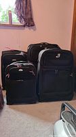 Four black Samsonite rolling suitcases visible together in the corner of a room, showing their relative sizes and overall condition needing cleaning.